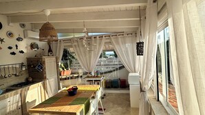 A spacious kitchen with a dining area, featuring a wooden ceiling, white walls, and a large window with curtains.