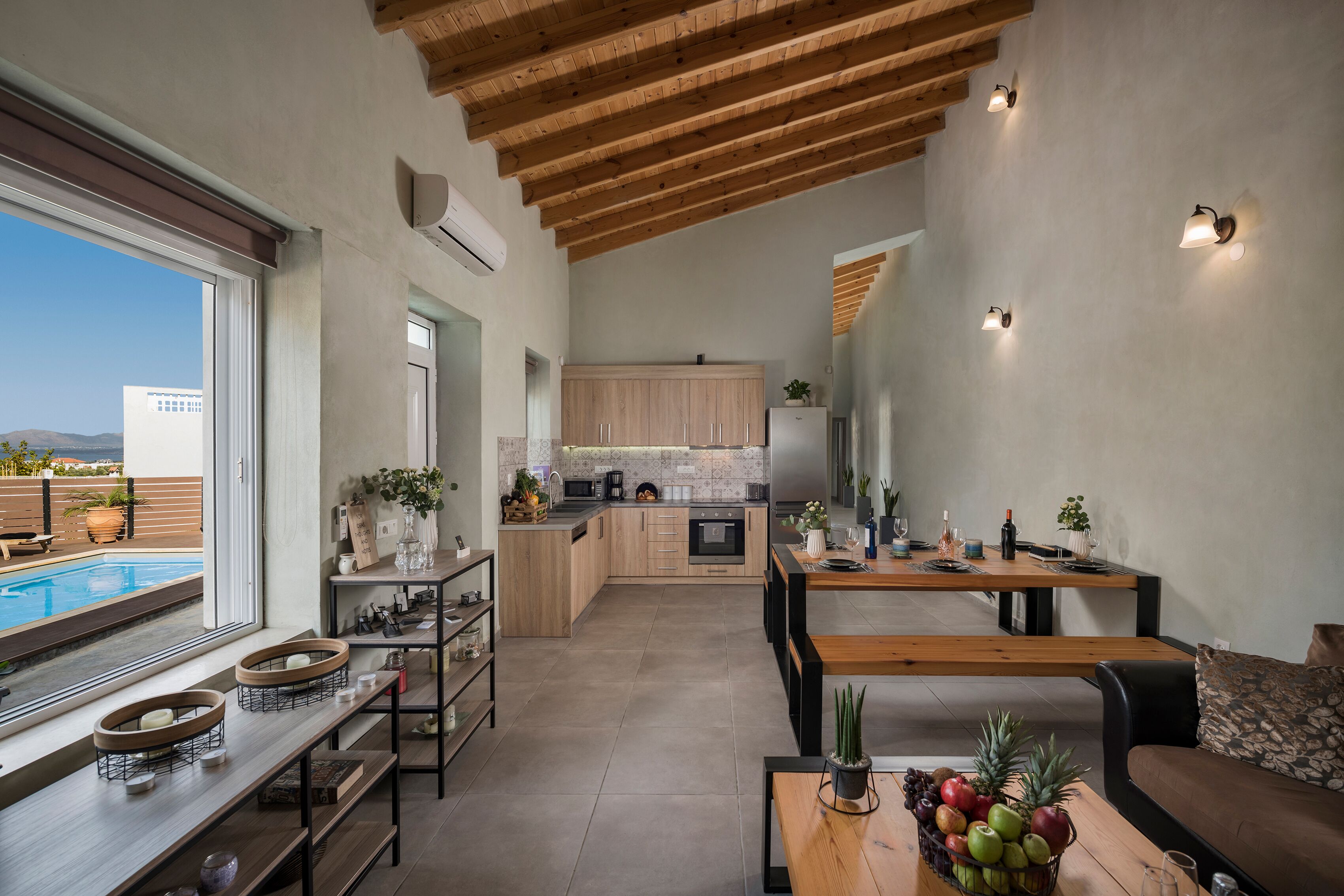 Una cucina moderna con mobili in legno, una zona pranzo con tavolo e panche, e vista su una piscina esterna.