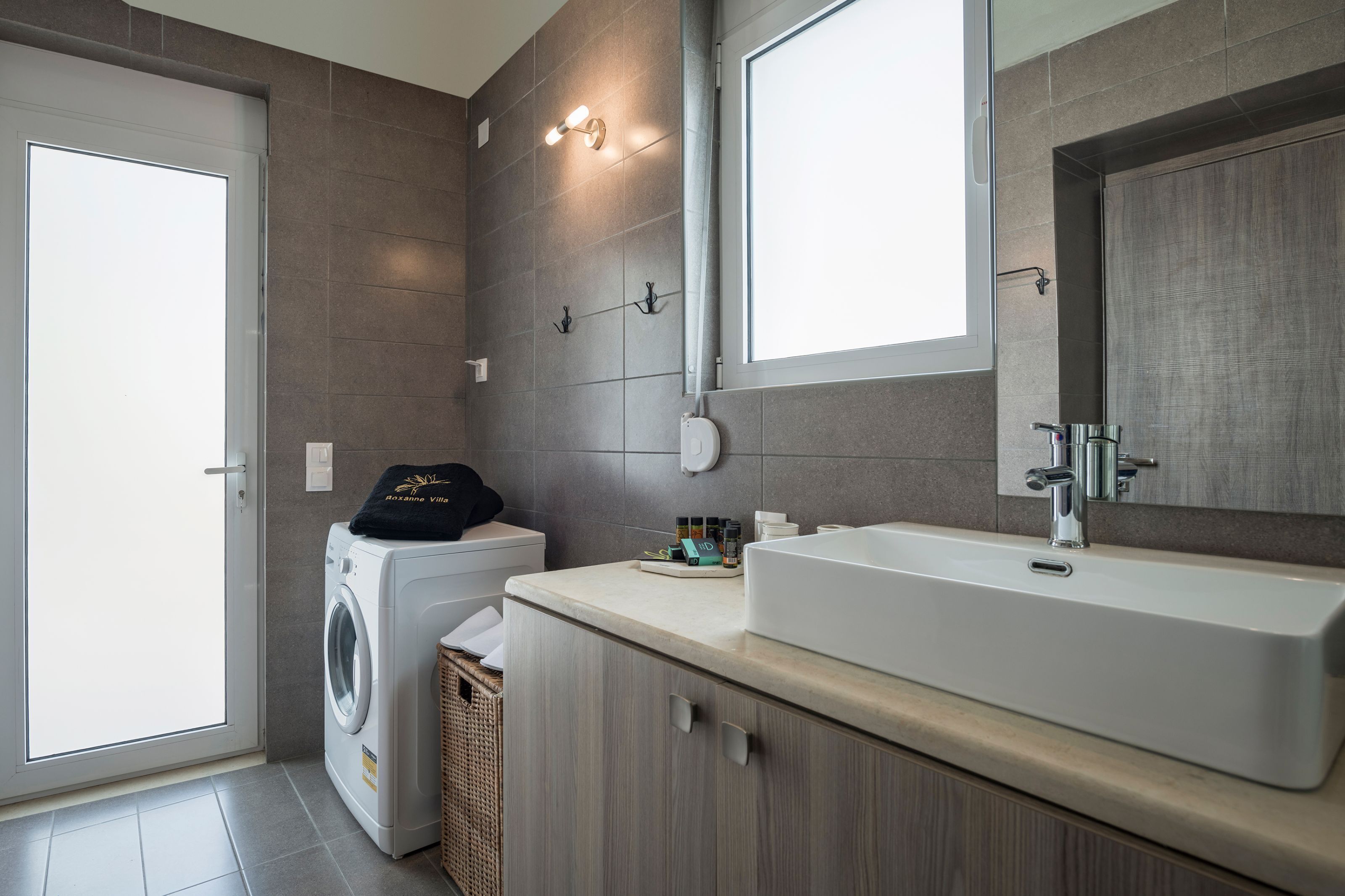 A modern bathroom with a large sink, a mirror, and a washing machine.