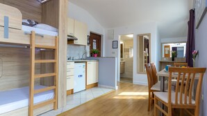 Un espace de vie compact comprenant un lit superposé, une kitchenette, un coin repas et une salle de bain.