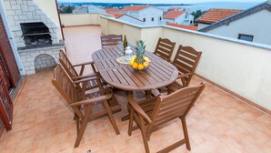 A round wooden table with chairs on a terrace with a view of buildings and the sea. - Apartment with Terrace and Partial Sea View and grill (Novalja)