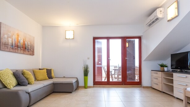 A modern living room with a grey sectional sofa, a flat-screen TV, and a dining area with a table and chairs. - Apartment with Terrace and Partial Sea View and grill (Novalja)