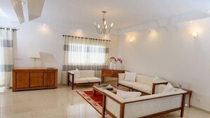 Amplia sala de estar con una mesa de centro de madera, dos sof ás blancos, un aparador de madera y una araña.