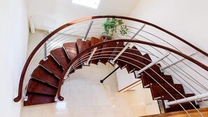 Una escalera de caracol con escalones de madera y barandillas metálicas, que sube a un piso superior.