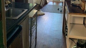 Cozinha compacta com pia, área de refeições com uma cadeira e vista para o exterior através de uma porta de vidro.