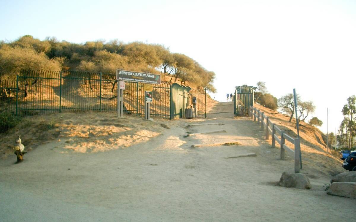 A dirt path leading to a gate at the entrance of a park with a sign reading "Runyon Canyon Park."