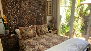Quarto com cama grande, cabeceira decorada e vista para o verde lá fora.