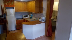 Een kleine keuken met houten kastjes, een magnetron, een koffiezetapparaat en een koelkast.