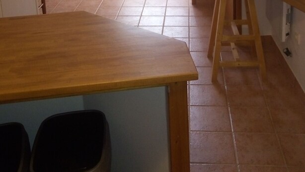 Een kamer met een plafondventilator, een eettafel, een houten bank, een bankstel en een raam met gordijnen.