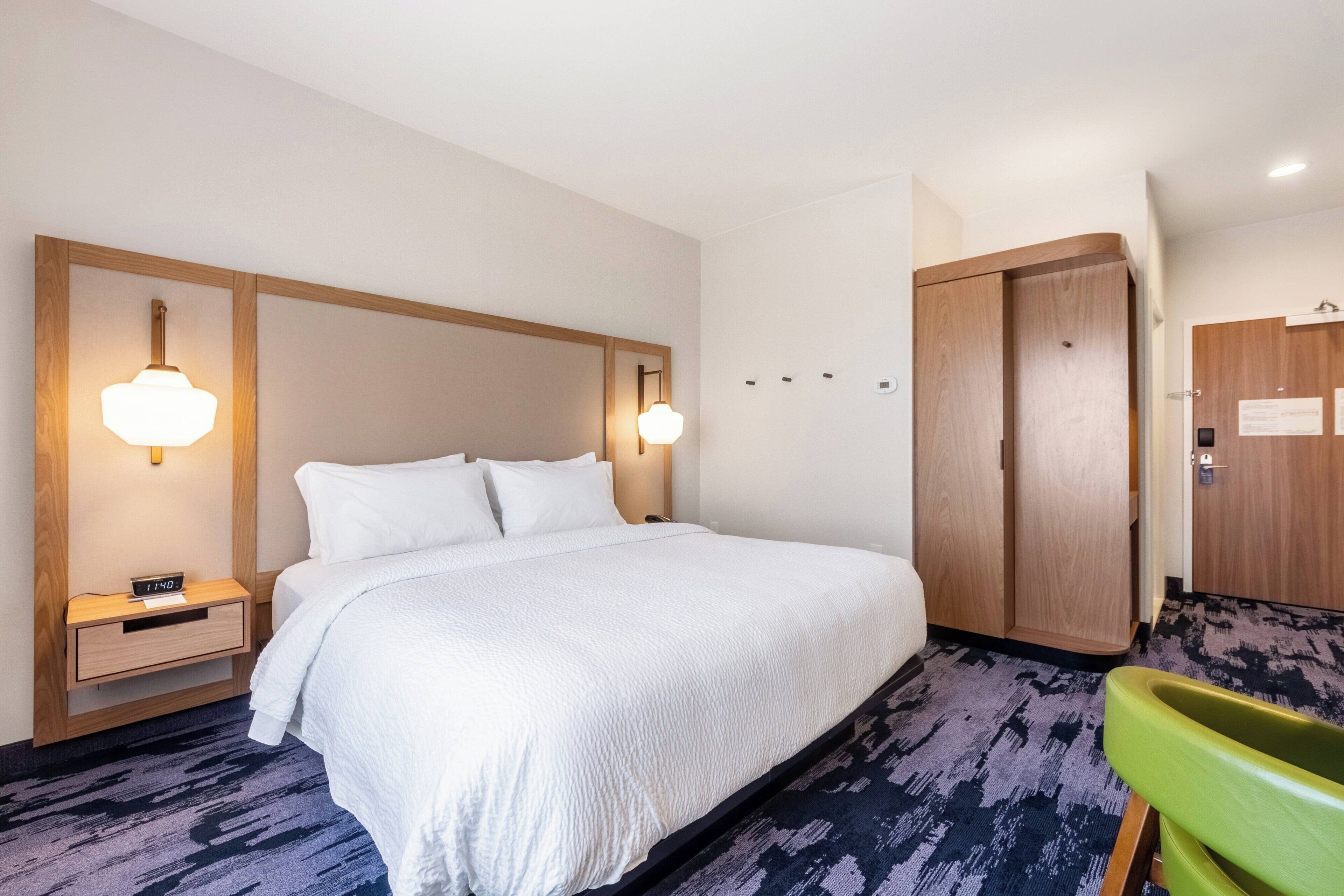 Habitación de hotel con una cama grande, mesitas de noche con lámparas, un armario de madera y una silla verde.