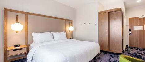 Habitación de hotel con una cama grande, mesitas de noche con lámparas, un armario de madera y una silla verde.