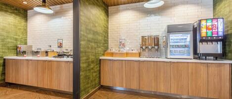 A modern reception area with wooden counters, a beverage dispenser, and a refrigerator.