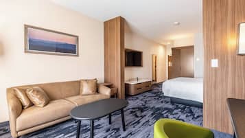 Ein Hotelzimmer mit einer Couch, einem kleinen Tisch, einem grünen Sessel, einem Bett, einem Fernseher und einem Holzschrank.