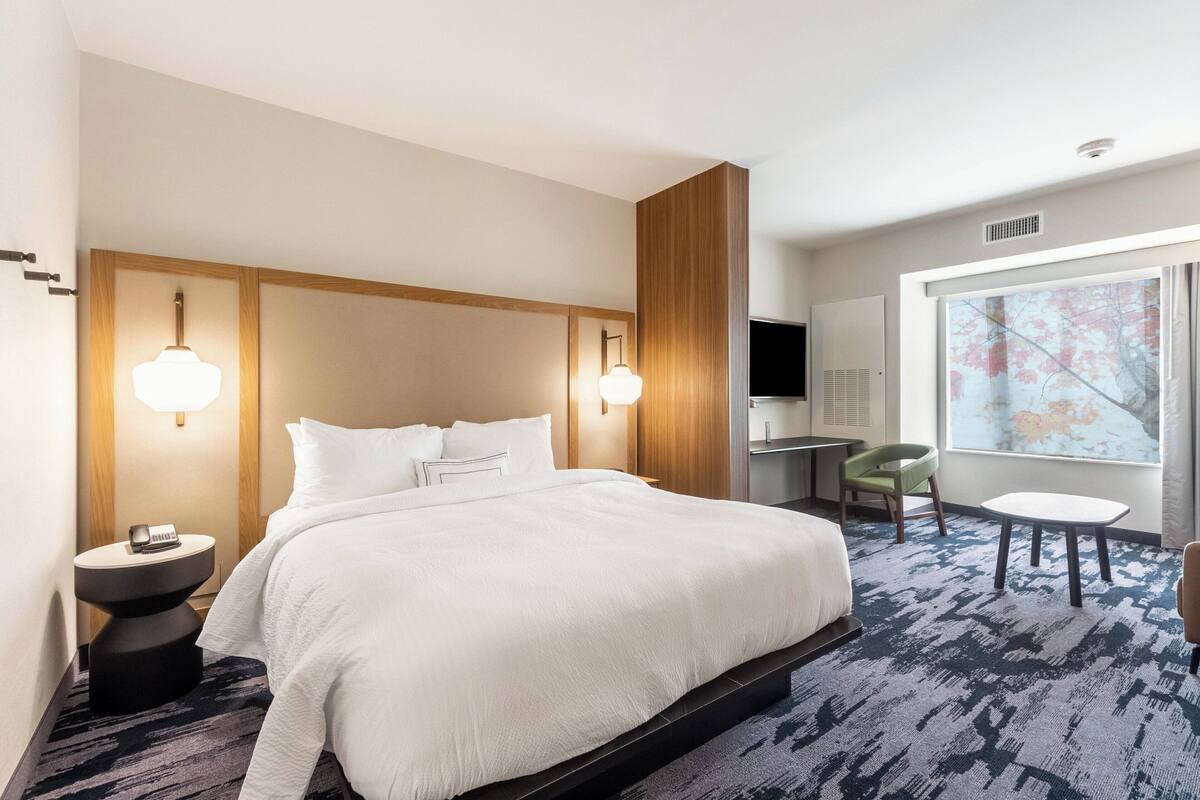 A hotel room with a large bed, bedside lamps, a desk, a chair, and a window with a view.