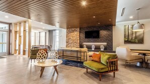 A spacious lobby with a wooden ceiling, a stone wall, and a flat-screen TV mounted above a reception desk.