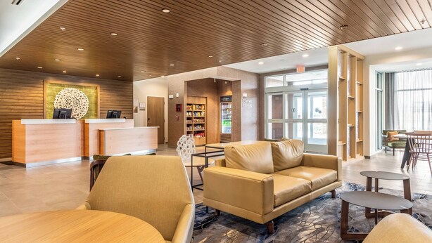 A modern lobby with a reception desk, leather seating, a coffee machine, and a bookshelf.