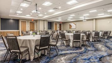 Un salón de conferencias con mesas redondas, sillas y piso alfombrado.