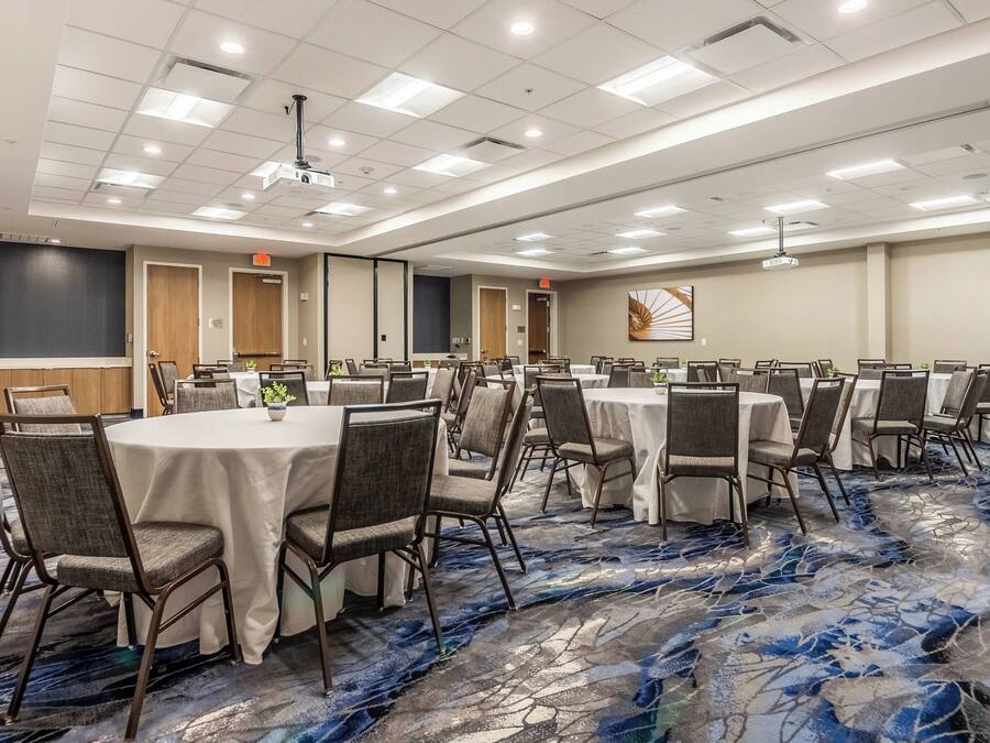 Un salón de conferencias con mesas redondas, sillas y piso alfombrado.