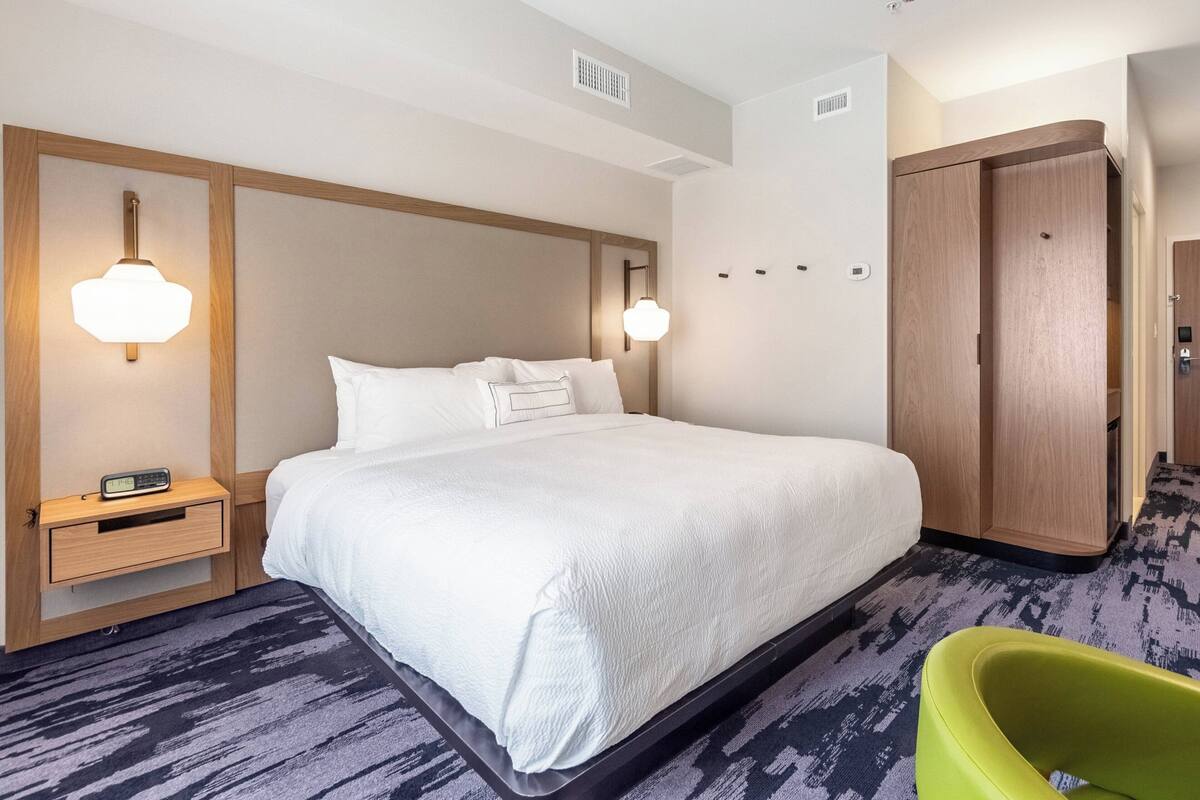 A hotel room with a large bed, bedside tables, a wardrobe, and a green chair.