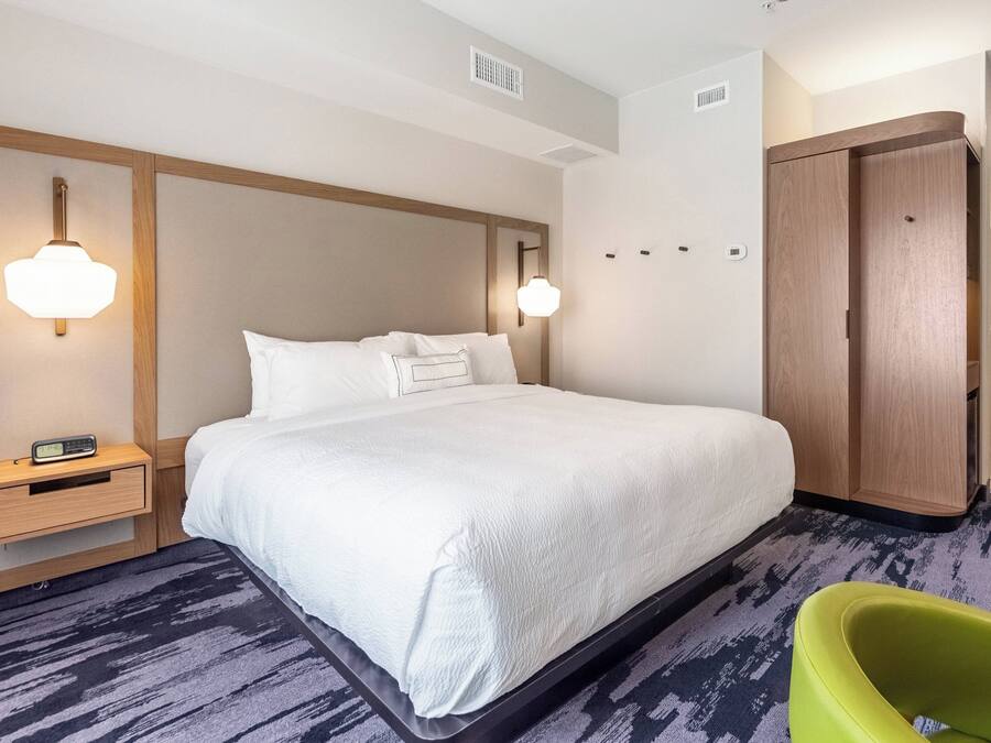 Una habitación de hotel con una cama grande, mesitas de noche, un armario y una silla verde.