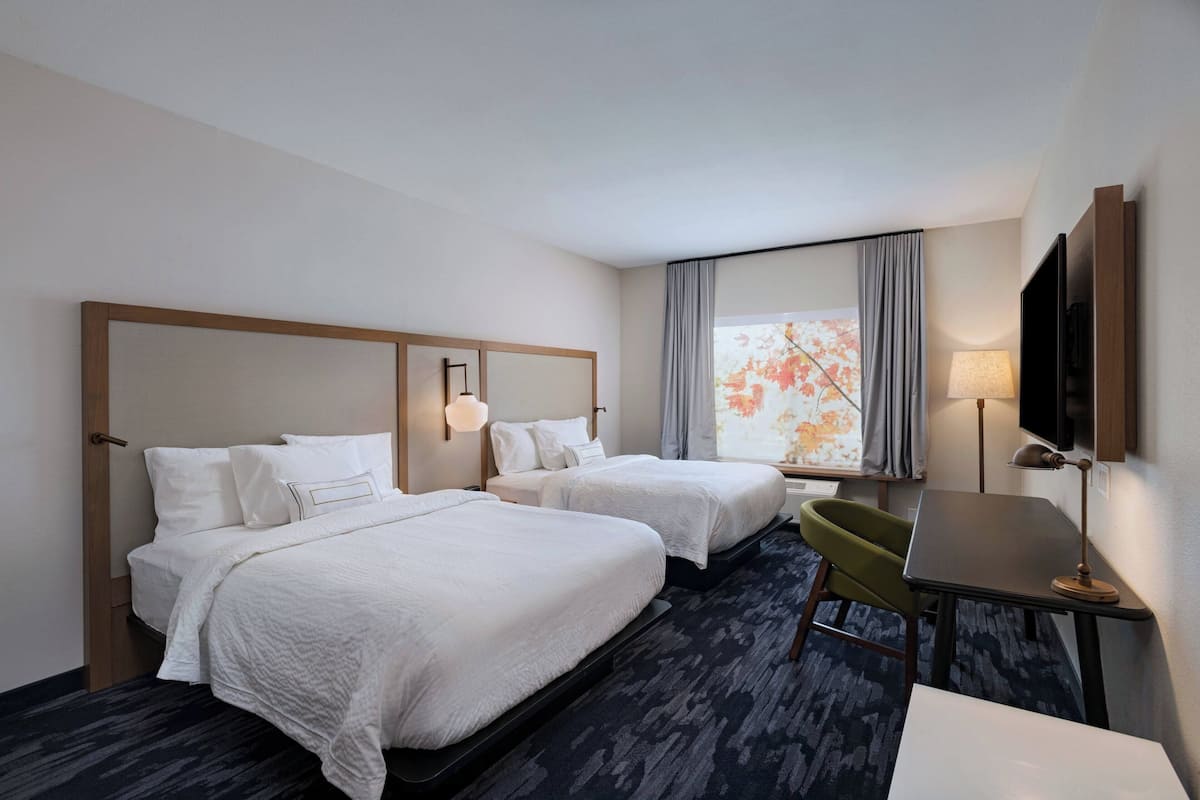 A hotel room with two beds, a desk, a chair, a TV, and a window with curtains.
