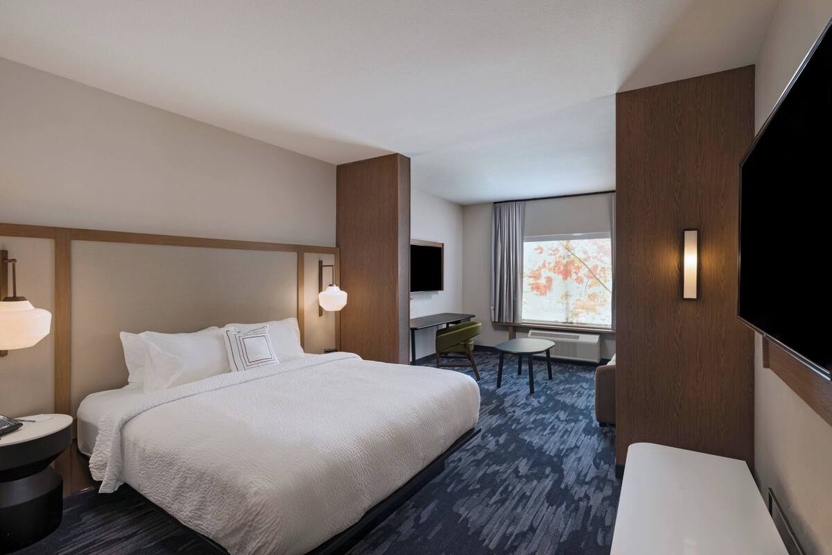 A hotel room with a large bed, a desk, a chair, a TV, and a window with a view.