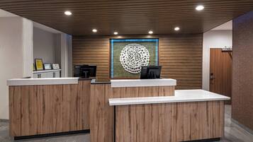 A reception area with wooden reception desks, a framed artwork on the wall, and a door to the right.