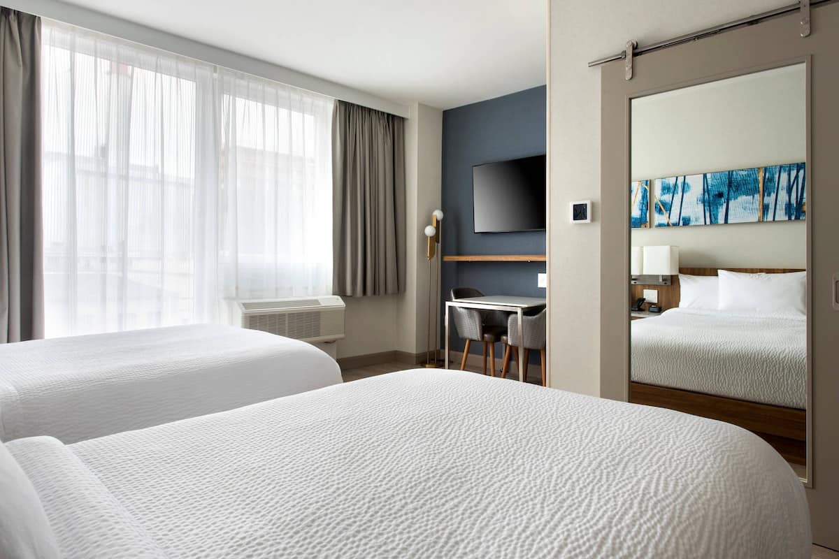 Une chambre d’hôtel avec deux lits, un bureau, une chaise, un téléviseur à écran plat et un grand miroir.