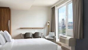 A hotel room with two beds, a desk, two chairs, a lamp, and a large window with curtains. - TownePlace Suites by Marriott New York Long Island City/Manhattan View (Long Island City)