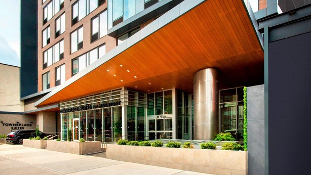 A modern hotel entrance with a glass facade, a wooden overhang, and a sign for 'Towneplace Suites'. - TownePlace Suites by Marriott New York Long Island City/Manhattan View (Long Island City)