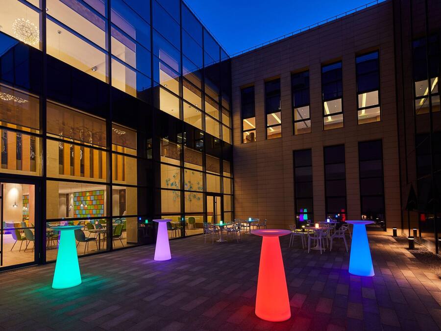 Un edificio moderno con grandes ventanales y un patio con mesas y sillas.