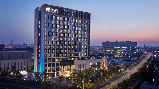 Un hotel moderno con una facciata luminosa, una griglia di finestre e un cartello 'aloft' ben visibile.