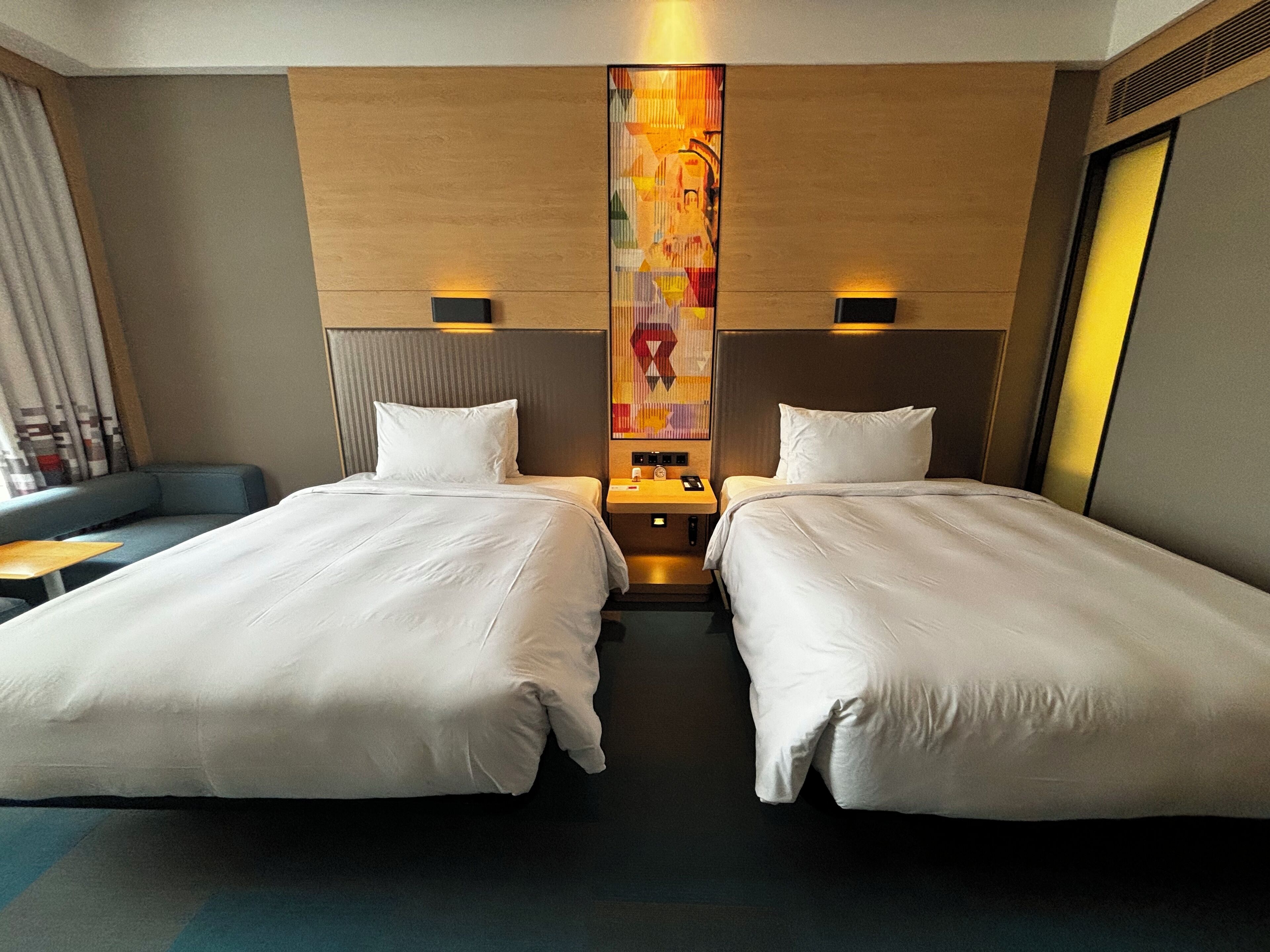 A hotel room with two beds, a sofa, a nightstand, and a wall art piece.