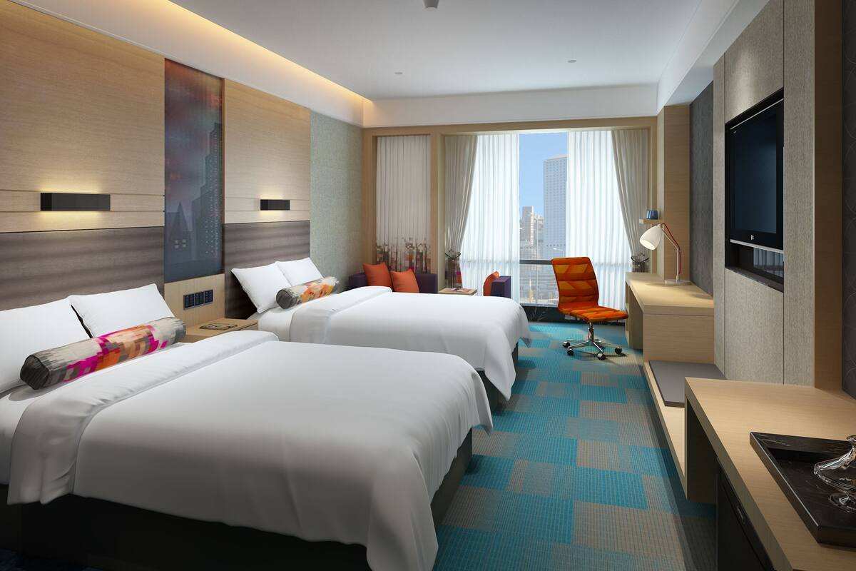 A modern hotel room with two beds, a desk, a chair, and a TV.