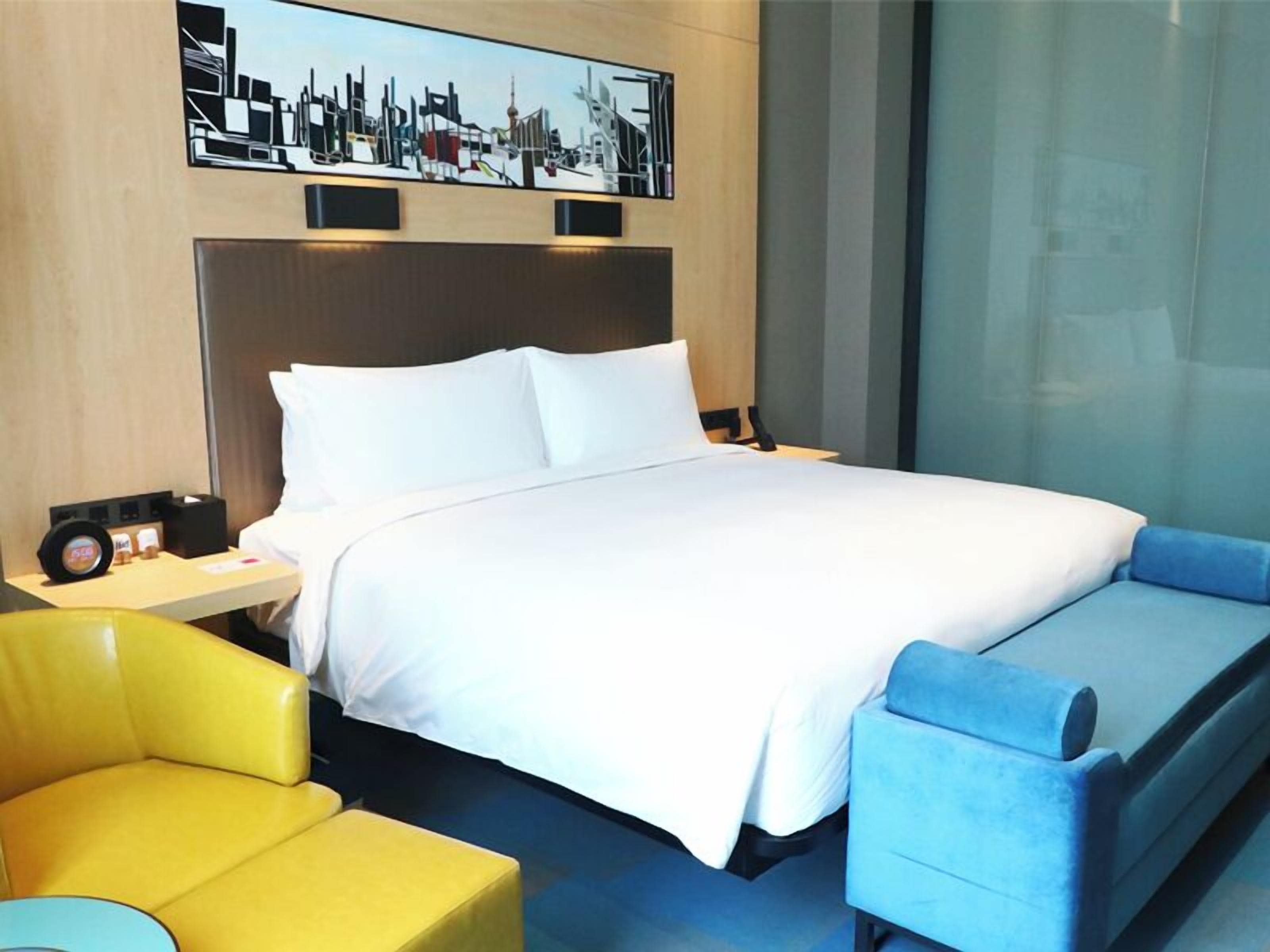 A hotel room with a bed, a nightstand, a yellow armchair, and a blue sofa.