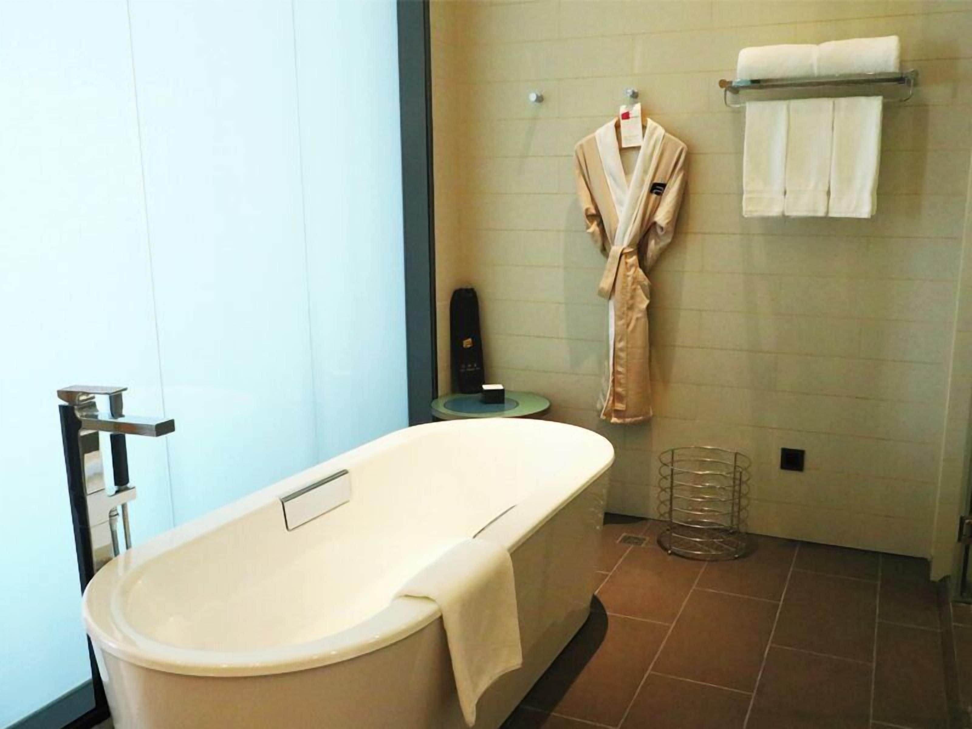 Een moderne badkamer met een vrijstaand bad, een handdoekrek met badjassen, en een klein tafeltje met een handdoekdispenser.
