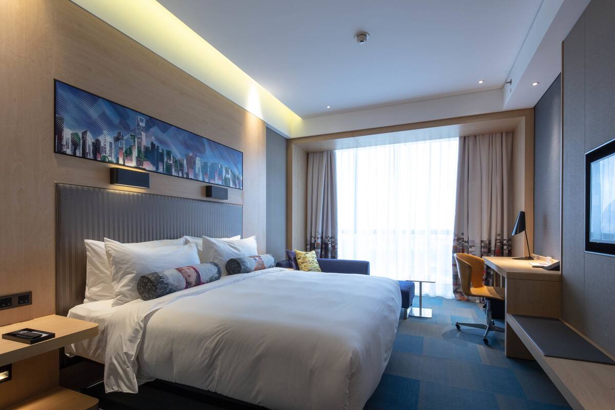 A modern hotel room with a large bed, a desk, and a television.