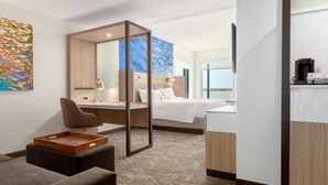 Una habitación de hotel moderna con cama, escritorio, silla, cafetera y vistas al mar.