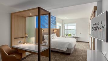 A modern hotel room with a large bed, a desk, a chair, and a TV.