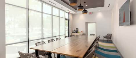 A conference room with a long wooden table, wicker chairs, and pendant lighting.