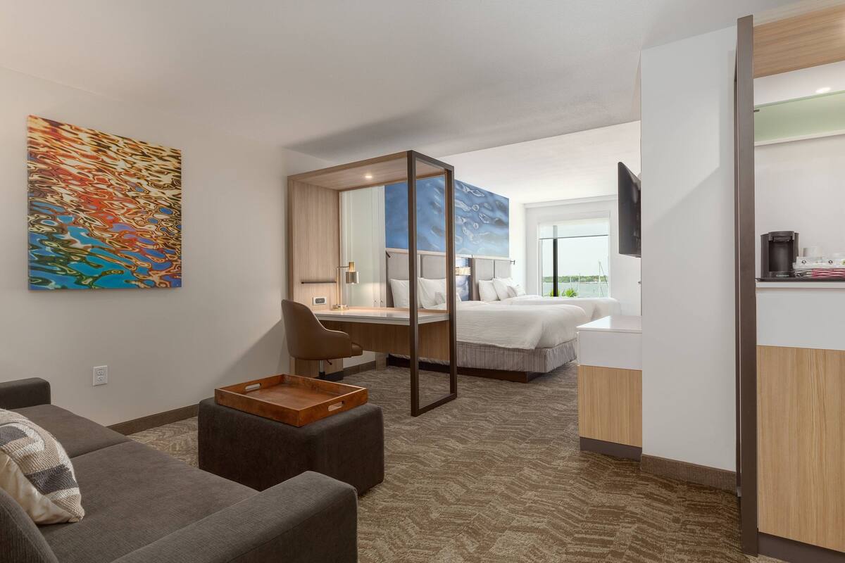 Una habitación de hotel moderna con sofá, escritorio, cama y un espejo grande.