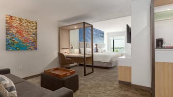 A modern hotel room with a sofa, a desk, a bed, and a large mirror.