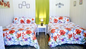 Una habitación con dos camas, cada una con ropa de cama floral, una mesita de noche con una lámpara y una cortina verde.