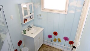 Un baño con un lavamanos blanco, un espejo y una ventana sobre el espejo.