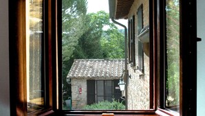 Una finestra con vista su un edificio in pietra con tetto in tegole e un piccolo giardino.