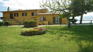 Un edificio giallo con una scalinata, aiuola e un albero.