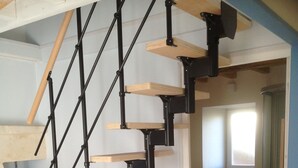 A staircase with wooden steps and black metal railings, leading to a room with a tiled floor and a door leading to another room. - La Maison de la Grève (Ouistreham)