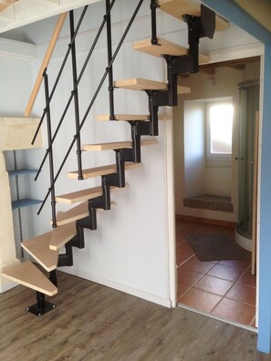 Eine Treppe mit Holzbodenstufen und schwarzen Metallgeländern, die zu einem Raum mit gefliestem Boden und einer Tür zu einem weiteren Raum führt.