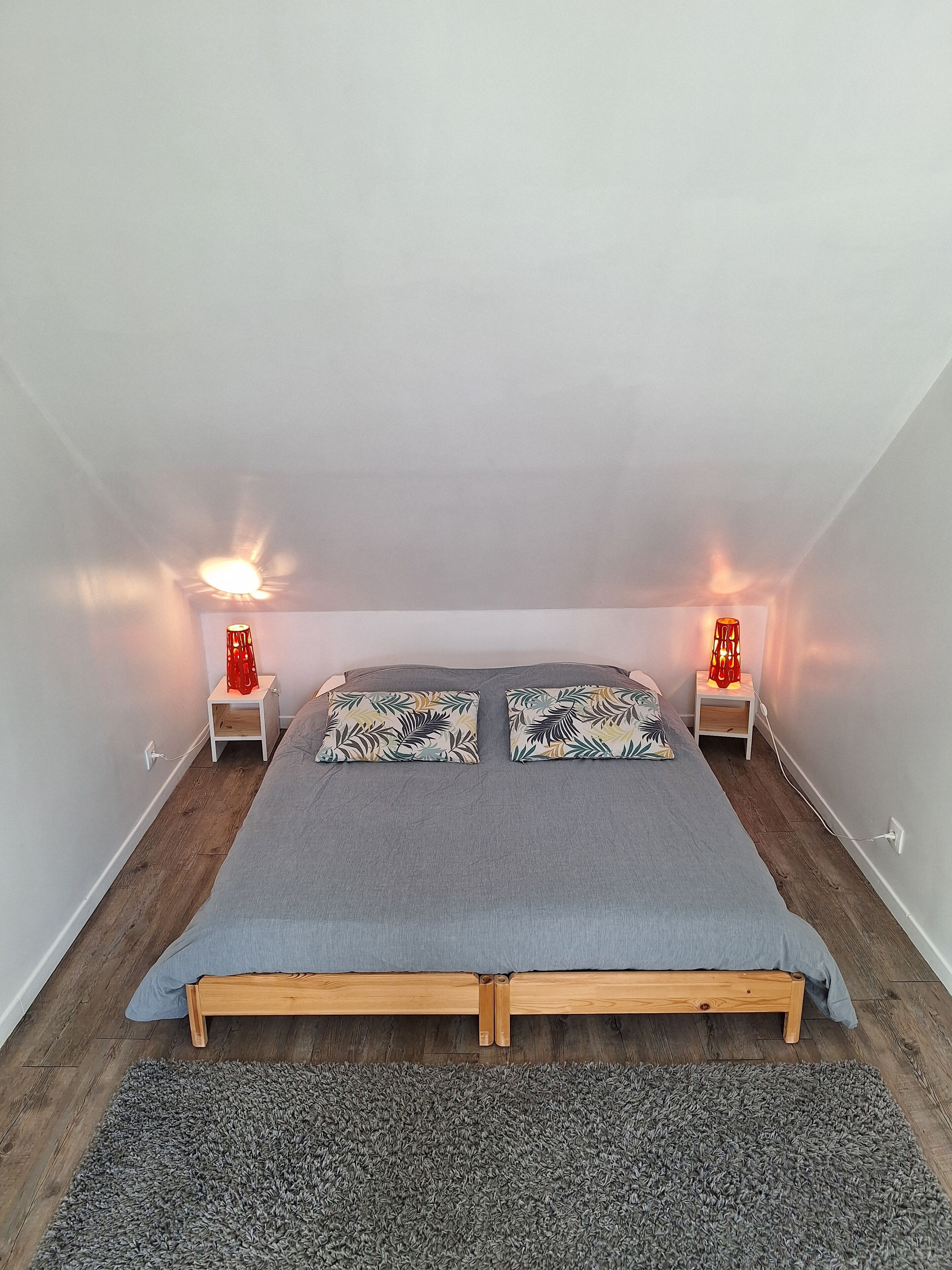 Une petite pièce bien éclairée, avec un lit simple, deux tables de chevet et un tapis.