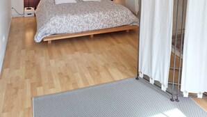 A bedroom with a wooden bed, a white ceiling light, a wall-mounted mirror, and a radiator. - La Maison de la Grève (Ouistreham)
